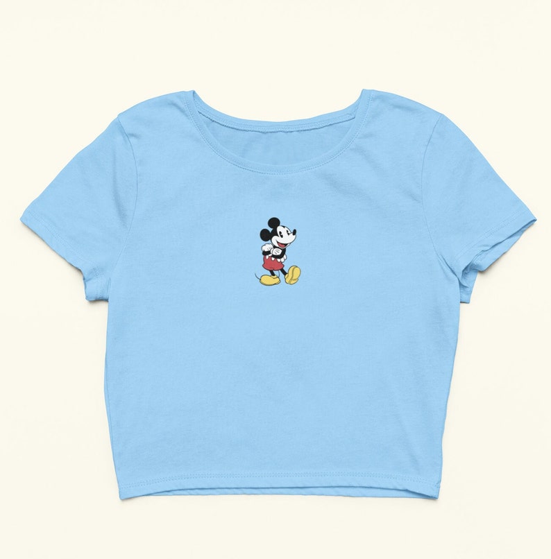 Peut inclure: Un t-shirt court bleu ciel avec une image de Mickey Mouse en dessin anim&eacute; au centre.