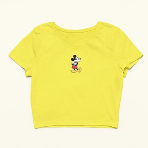 Peut inclure: Un t-shirt jaune court avec une petite image brod&eacute;e de Mickey Mouse marchant.