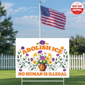 May include: A white yard sign with the words "ABOLISH ICE" and "NO HUMAN IS ILLEGAL" in orange text, decorated with flowers. An American flag waves in the background under a blue sky.