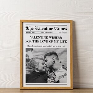 May include: A framed print resembling a newspaper front page, titled "The Valentine Times." The headline reads "VALENTINE WISHES: FOR THE LOVE OF MY LIFE." A black and white photo shows a couple kissing. The frame is a light brown color.