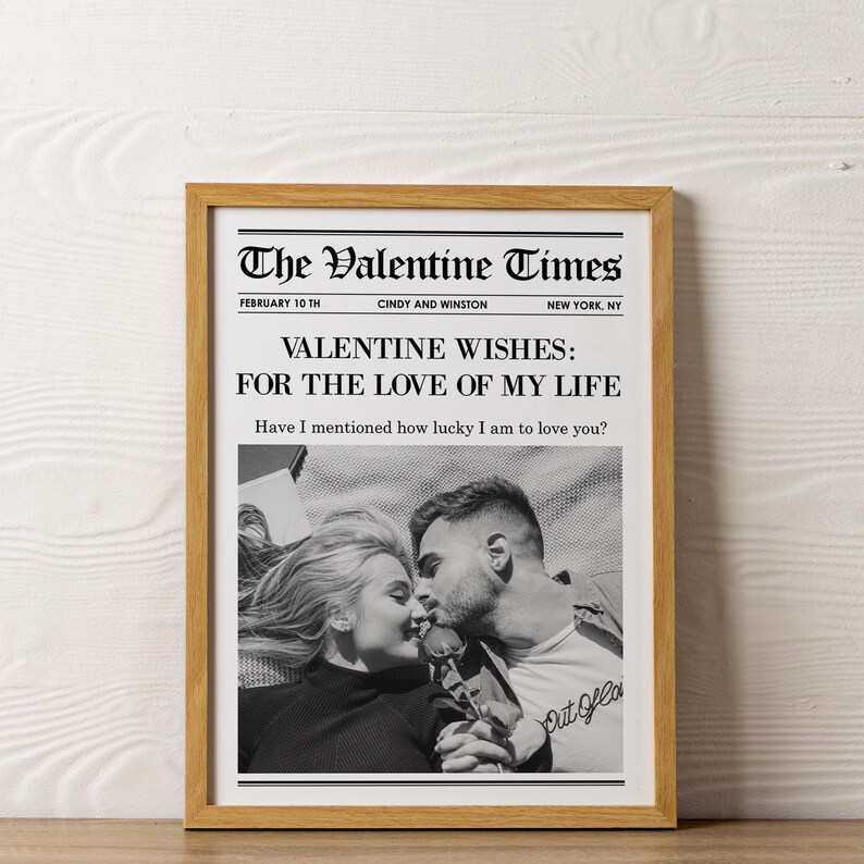 May include: A framed print resembling a newspaper front page, titled "The Valentine Times." The headline reads "VALENTINE WISHES: FOR THE LOVE OF MY LIFE." A black and white photo shows a couple kissing. The frame is a light brown color.