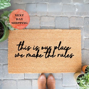 May include: A brown coir doormat with the text "This is our place we make the rules" in black cursive lettering.
