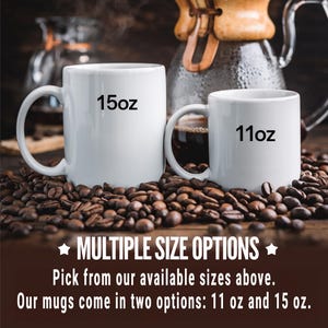 May include: Two white ceramic mugs with black text. The larger mug says "15oz" and the smaller mug says "11oz". Both mugs are sitting on a bed of coffee beans.