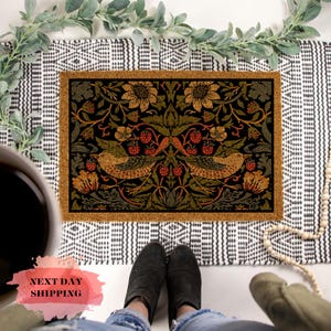 May include: A brown coir doormat with a black and gold floral design featuring two birds and berries. The design is reminiscent of a vintage tapestry.