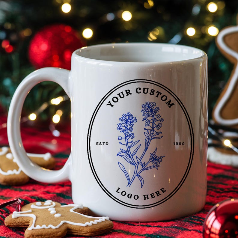 May include: White ceramic mug with a black and blue logo featuring a floral design. The logo reads "Your Custom Logo Here" with "Estd 1990" below the floral design.