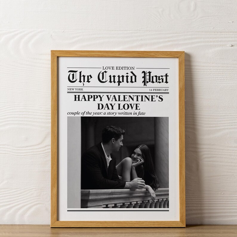 May include: A framed black and white photograph with a wooden frame. The image is a newspaper-style print titled "The Cupid Post" with the headline "Happy Valentine's Day Love." The photograph features a couple looking at each other.