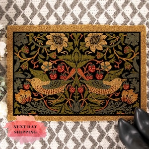 May include: A coir doormat with a black background and a floral pattern featuring birds, leaves, and berries. The pattern is in shades of green, yellow, orange, and red.