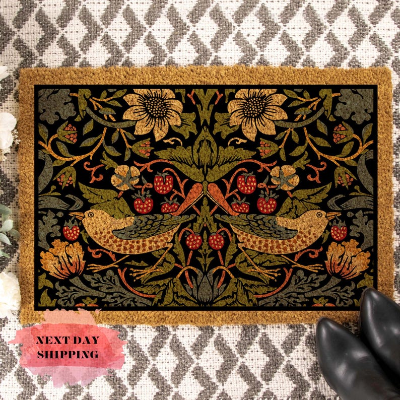 May include: A coir doormat with a black background and a floral pattern featuring birds, leaves, and berries. The pattern is in shades of green, yellow, orange, and red.