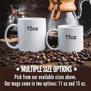 May include: Two white ceramic mugs with black text. The larger mug says "15oz" and the smaller mug says "11oz". Both mugs are sitting on a bed of coffee beans.