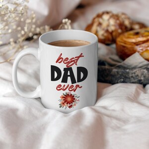 May include: White ceramic coffee mug with a black and red design that says "best dad ever" with a floral design at the bottom.