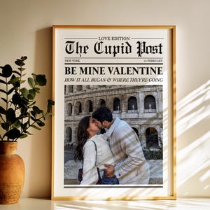 May include: A framed print with a gold border featuring a couple kissing in front of a historic building. The print is designed to look like a newspaper front page, with the headline "The Cupid Post" and the text "Be Mine Valentine."