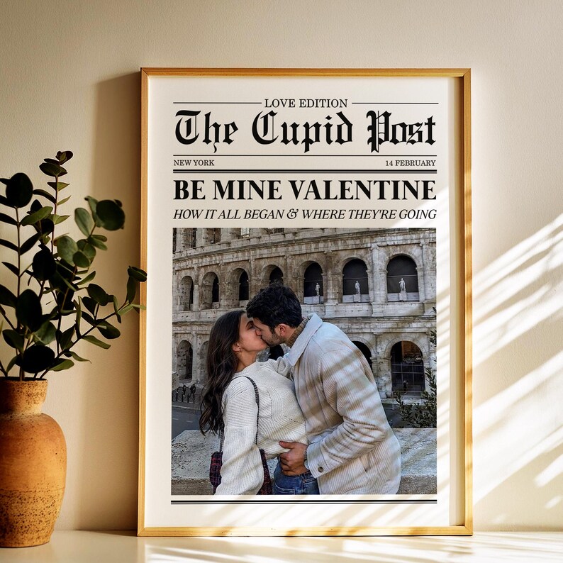May include: A framed print with a gold border featuring a couple kissing in front of a historic building. The print is designed to look like a newspaper front page, with the headline "The Cupid Post" and the text "Be Mine Valentine."