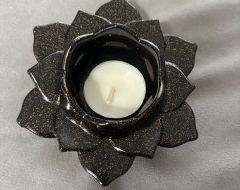 Puede incluir: Portavelas de color negro con purpurina dorada en forma de flor de loto. El portavelas tiene una pequeña hendidura redonda en el centro para sostener una vela de té.