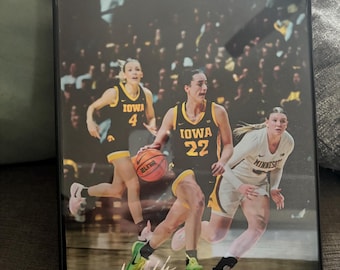 May include: A framed photograph of three women's basketball players in action. The players are wearing black and gold uniforms with the word "Iowa" on the front. The player in the center is holding a basketball and has the number "22" on her jersey. The player on the left has the number "4" on her jersey. The player on the right has the number "23" on her jersey. The photograph is signed "Curt Cole".