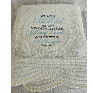 May include: A white quilted blanket with a blue embroidered quote that reads "You are a Child of God. You are wonderfully made, dearly loved and precious in His sight. Psalm 139."