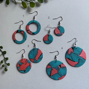May include: A selection of handmade earrings in different shapes and sizes. The earrings have a teal and coral colour scheme with a marbled effect. Some are circular, others are round, and all have silver hooks.