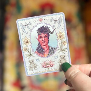 May include: A whimsical illustration of a fantasy character with horns and red skin. The character is surrounded by flowers, butterflies, and teddy bears. The image has a pastel colour palette and a whimsical style.