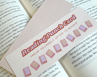 Puede incluir: Una tarjeta perforada de lectura rosa con el texto "Reading Punch Card" y "Treat Yourself After 10 Books!" se muestra sobre un libro abierto. La tarjeta presenta ilustraciones de libros. La tarjeta es una recompensa por leer.