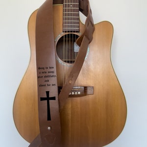 May include: Brown leather guitar strap with an engraved cross and the text "Sing to him a new song: play skillfully, and shout for joy."