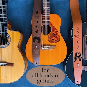 May include: Three different guitars with guitar straps featuring various designs. The straps are black, brown, and orange. The straps have the words "Elvis", "Awake", and "One Love" printed on them. The guitars are a classical guitar, an acoustic guitar, and an electric guitar.