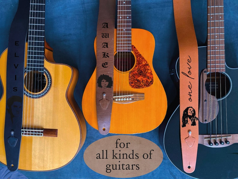 May include: Three different guitars with guitar straps featuring various designs. The straps are black, brown, and orange. The straps have the words "Elvis", "Awake", and "One Love" printed on them. The guitars are a classical guitar, an acoustic guitar, and an electric guitar.