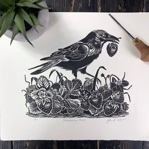 May include: A black and white linocut print of a crow holding a strawberry in its beak. The crow is standing in a field of strawberry plants. The print is signed "Jared. Soto" and numbered "3/50".