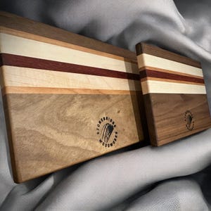 May include: Two wooden chopping boards with a striped pattern of light and dark wood. The larger board has a logo that says "Stonebridge Woodworks".