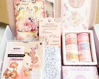 May include: A pink and white box filled with craft supplies, including stickers, washi tape, and a journal. The box has the words "Flower of Fun" and "Dreamland" printed on it.