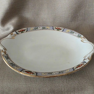 May include: A white oval serving dish with a blue, gold, and red floral design around the rim.