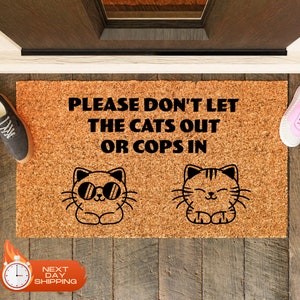 May include: A brown coir doormat with the text "PLEASE DON'T LET THE CATS OUT OR COPS IN" in black. Two black and white cartoon cats are on either side of the text. The cat on the left is wearing sunglasses.
