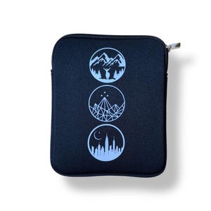 Puede incluir: Bolsa negra con cremallera y tres c&iacute;rculos azules. Cada c&iacute;rculo presenta un dise&ntilde;o diferente: monta&ntilde;as con un ciervo, una monta&ntilde;a geom&eacute;trica con estrellas y un horizonte urbano con una luna creciente.