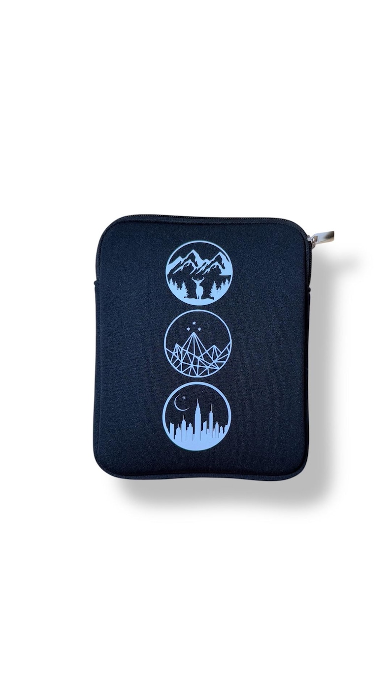 Puede incluir: Bolsa negra con cremallera y tres c&iacute;rculos azules. Cada c&iacute;rculo presenta un dise&ntilde;o diferente: monta&ntilde;as con un ciervo, una monta&ntilde;a geom&eacute;trica con estrellas y un horizonte urbano con una luna creciente.