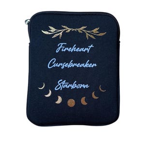 Puede incluir: Bolsa negra con cremallera con detalles en pan de oro y el texto "Fireheart Cursebreaker Starborn" en letras azules. La bolsa tiene un dise&ntilde;o de media luna dorada.