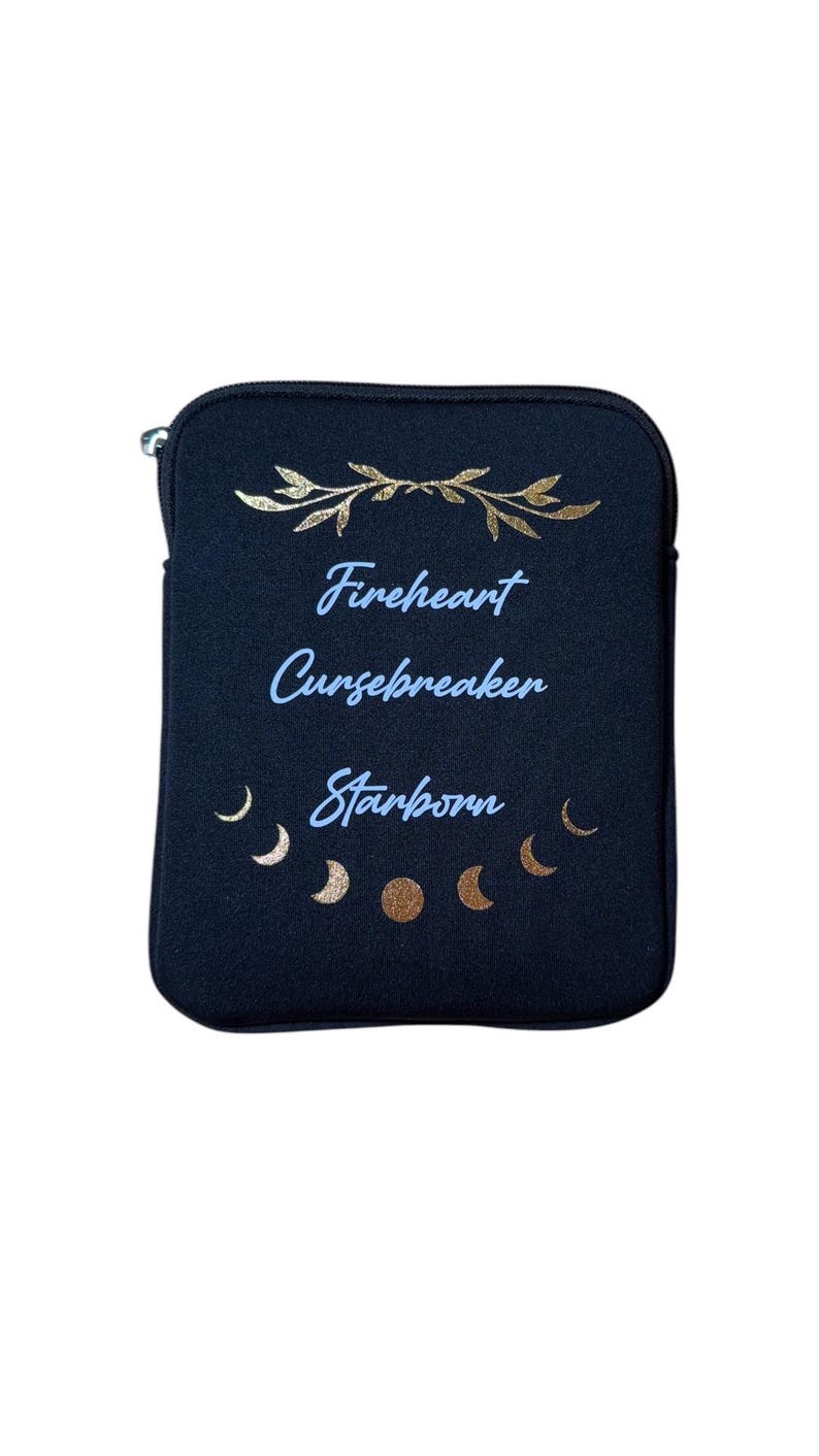 Puede incluir: Bolsa negra con cremallera con detalles en pan de oro y el texto "Fireheart Cursebreaker Starborn" en letras azules. La bolsa tiene un dise&ntilde;o de media luna dorada.