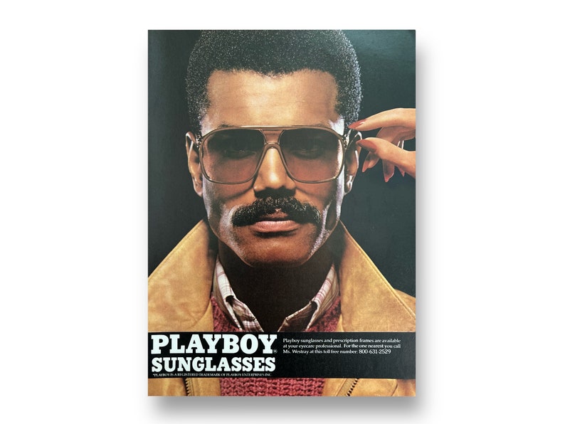 A vintage Playboy Sunglasses ad shows a man in sunglasses and a mustache. A hand with red nails reaches over to take the glasses off. The man is wearing a red sweater and suede 80s jacket. Beneath him reads, Playboy Sunglasses.