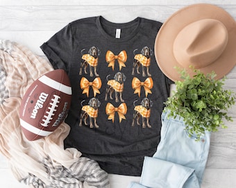 May include: A dark gray t-shirt with a pattern of black and brown dogs wearing orange bows. The dogs are repeated throughout the shirt.