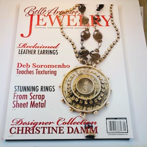 May include: The front cover of Belle Armoire Jewelry magazine features a large circular pendant with a number 3 typewriter key center, surrounded by rhinestones and black beads. Text includes Reclaimed Leather Earrings and Stunning Rings.