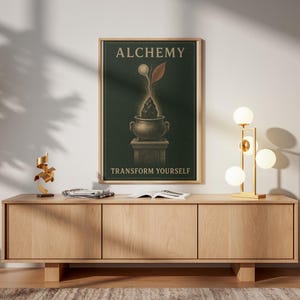 Può includere: Una stampa artistica incorniciata con sfondo verde scuro che riporta la parola ALCHEMY in alto e TRANSFORM YOURSELF in basso. L'illustrazione centrale raffigura una pietra scura all'interno di un calderone su un piedistallo con una foglia e un globo.