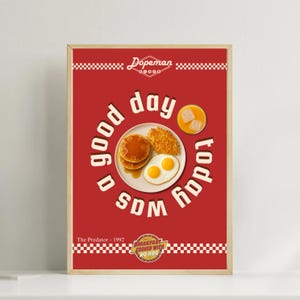 May include: A framed print with a red background featuring a breakfast plate with pancakes, eggs, and hash browns. The text "good day today was a SDM" is in a circle around the plate. The print also includes the text "Dopeman" and "The Predator - 1992".