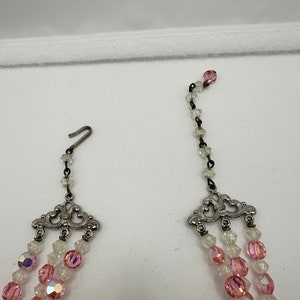 May include: A multi-strand necklace with pink and clear glass beads. The necklace has a silver clasp and decorative silver accents.