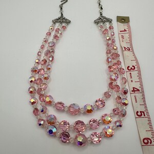 May include: A three-strand pink and clear crystal necklace with a silver clasp. The necklace is approximately 15 inches long.