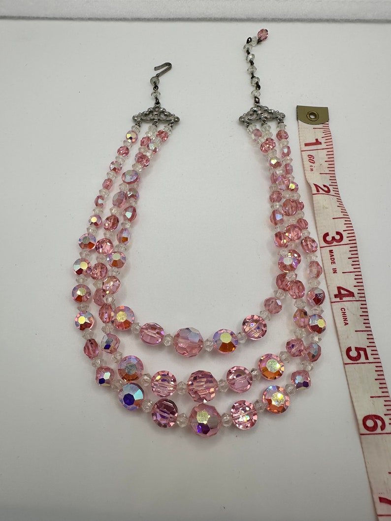 May include: A three-strand pink and clear crystal necklace with a silver clasp. The necklace is approximately 15 inches long.