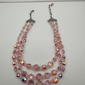 May include: A three-strand pink crystal necklace with silver clasps. The necklace features iridescent pink and clear crystal beads.