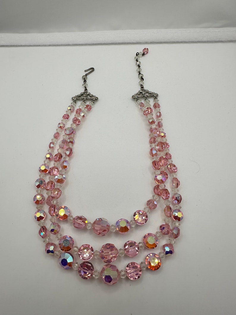 May include: A three-strand pink crystal necklace with silver clasps. The necklace features iridescent pink and clear crystal beads.