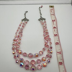 May include: A three-strand pink crystal necklace with a silver clasp. The necklace is approximately 7 inches long.