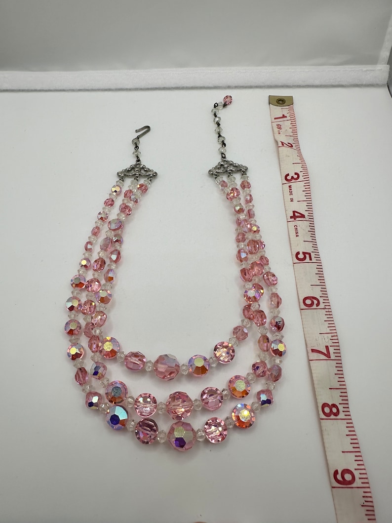 May include: A three-strand pink crystal necklace with a silver clasp. The necklace is approximately 7 inches long.