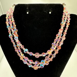 May include: A three-strand iridescent pink crystal bead necklace. The beads are faceted and have a clear center with a pink outer layer.
