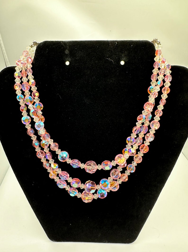 May include: A three-strand iridescent pink crystal bead necklace. The beads are faceted and have a clear center with a pink outer layer.
