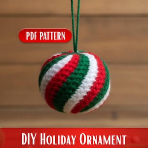 May include: A crocheted holiday ornament with red, white, and green stripes, suspended by a green string. The ornament has a spherical shape. Text on the image reads "PDF PATTERN" and "DIY HOLIDAY ORNAMENT".