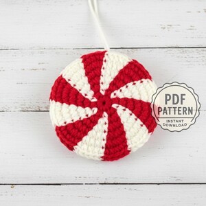 Può includere: Ornamento fatto a mano, all'uncinetto, a forma di caramella alla menta. L'ornamento presenta strisce rosse e bianche alternate, con un cordino bianco per appenderlo. Il testo "PDF PATTERN" e "INSTANT DOWNLOAD" è visibile.
